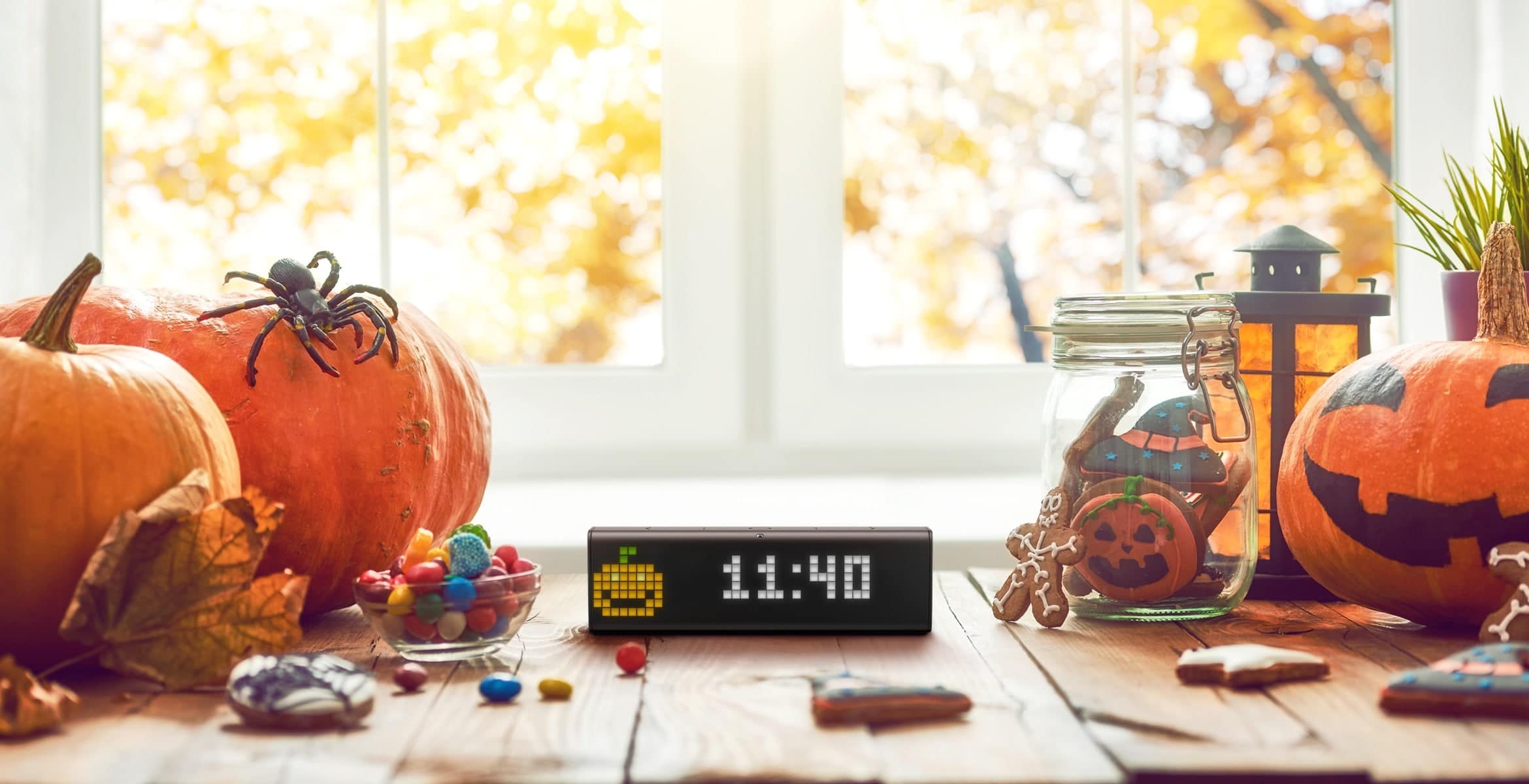 LaMetric Time smart clock displays time and a pumpkin clock face, standing on a table with Halloween decorations